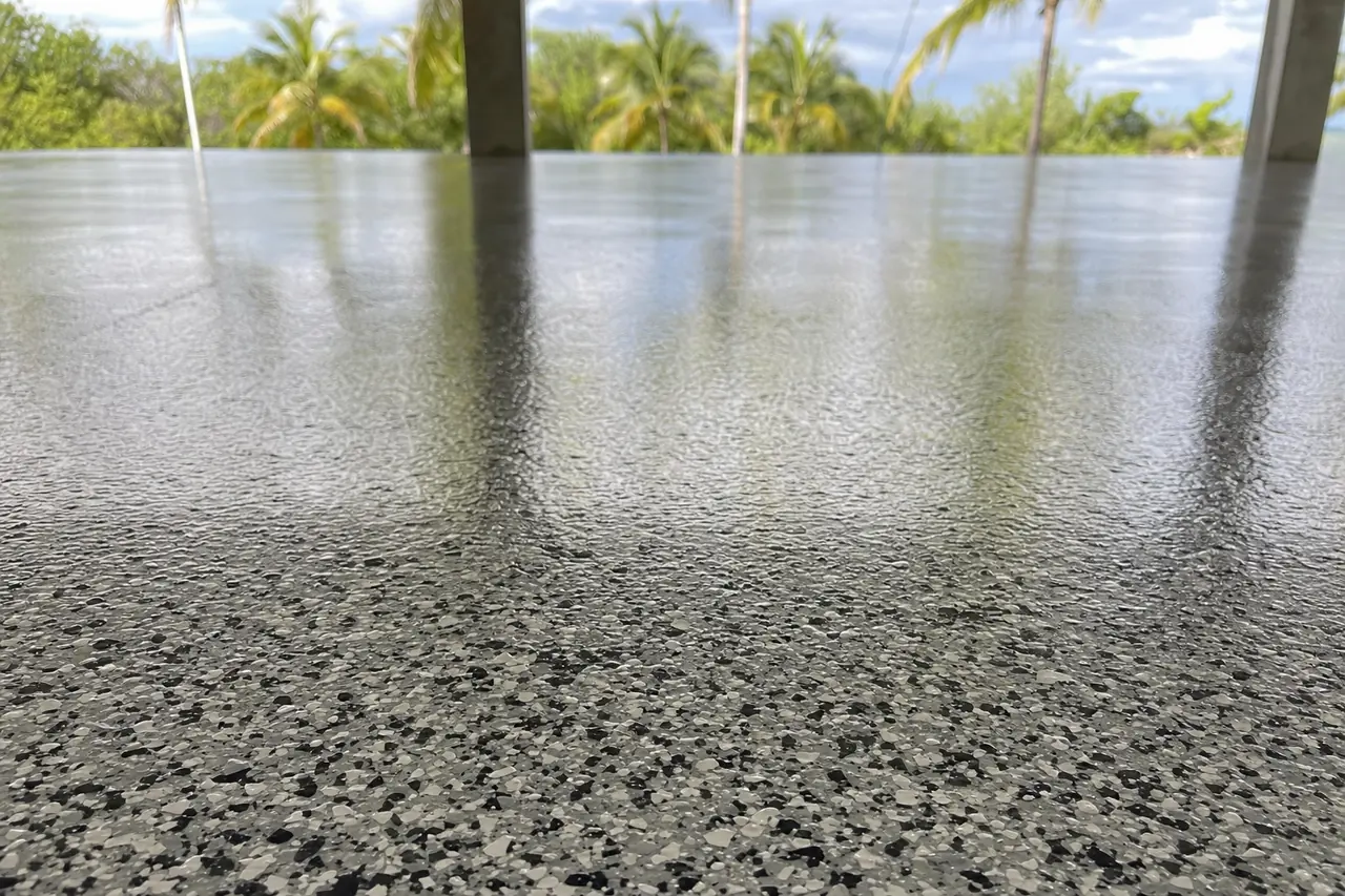 A bare concrete carport slab under a roof with palms in strong tropical light — epoxy floor coatings, Darwin. Illustrative example.