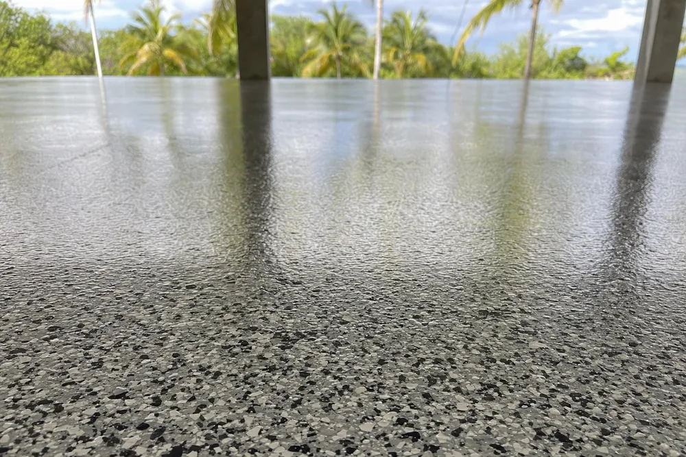 A bare concrete carport slab under a roof with palms in strong tropical light — epoxy floor coatings, Darwin. Illustrative example.